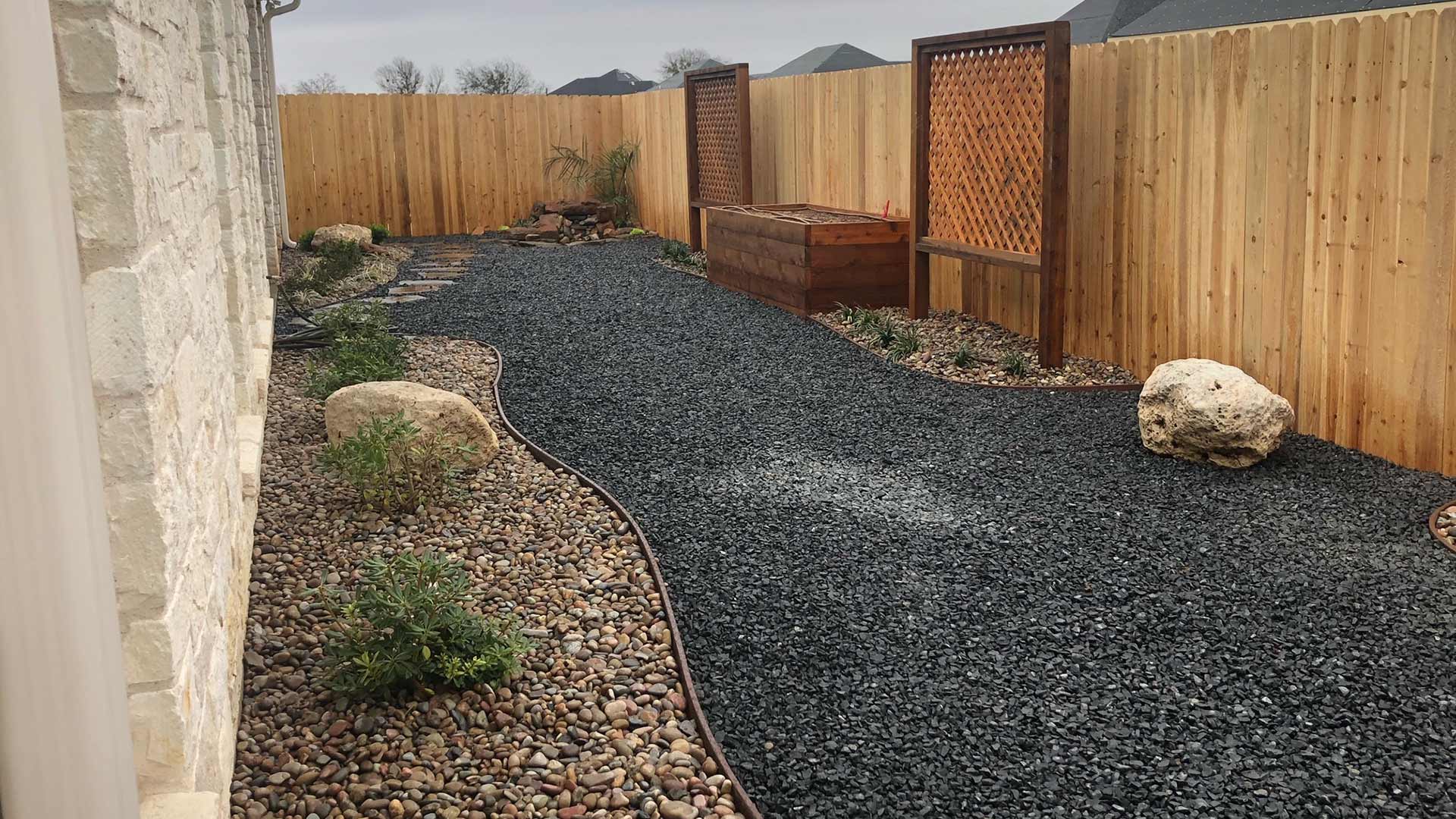 Landscaping with rock mulch and wooden fence around a home in China Spring, TX.