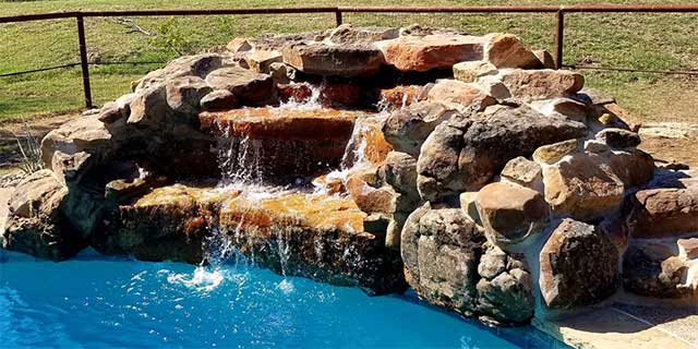 Rock and boulder water feature with waterfall by a pool in Hewitt, TX.