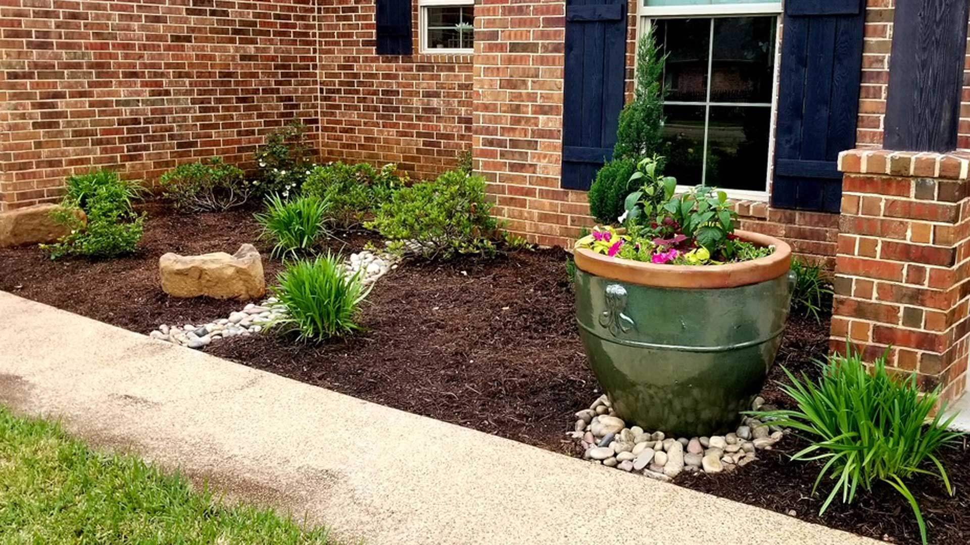 Landscape bed with drainage solution, plantings, and potted plant installed in China Spring, TX.