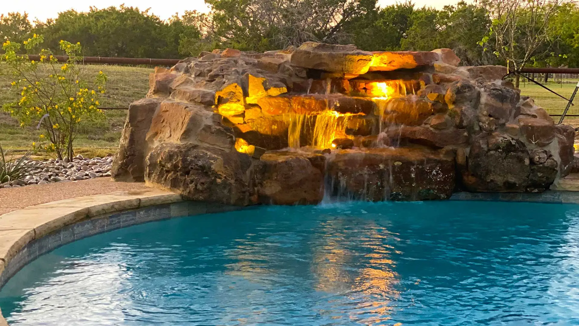 Waterfall water feature with landscape lighting installed by a pool in Waco, TX.