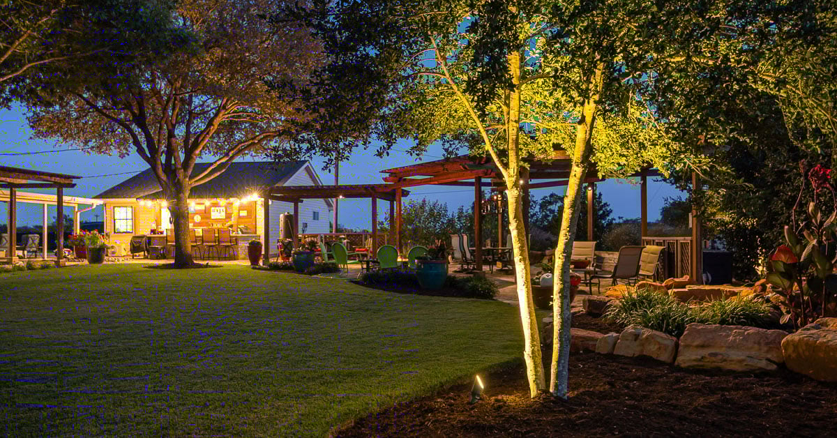 Backyard tree lighting up lighting pergola green lawn outdoor kitchen 