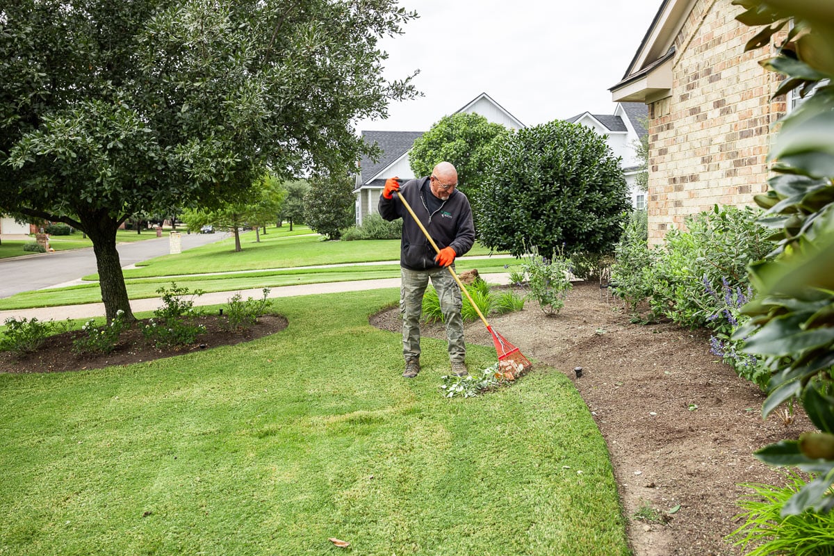 Landscape maintenance crew raking landscape beds cleaning up