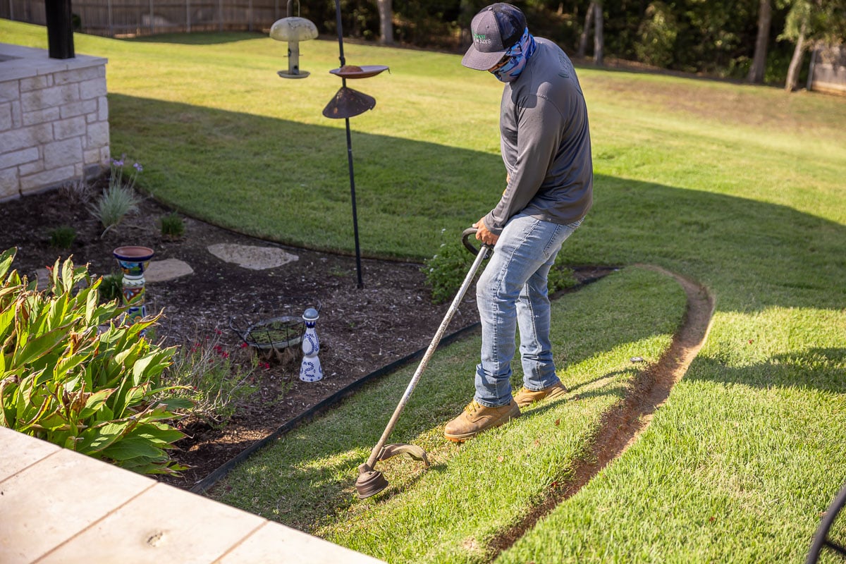 Residential landscape maintenance crew weed wacking backyard patio green lawn 
