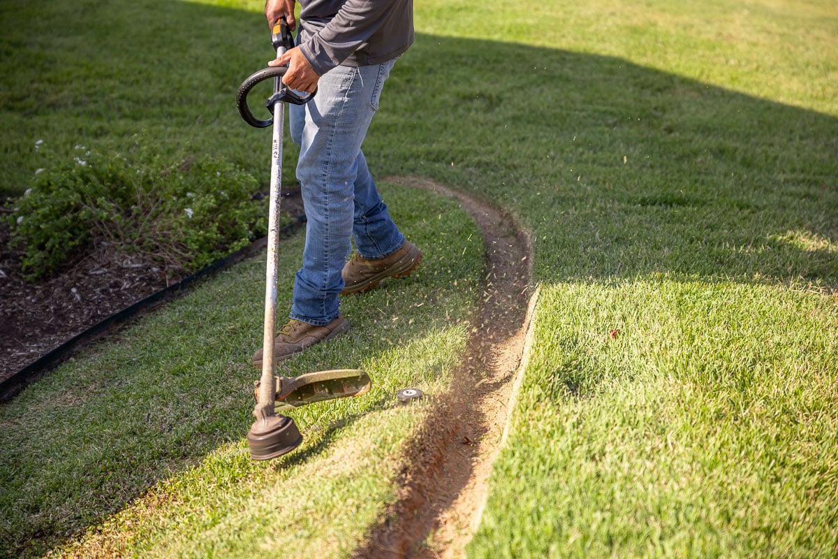 Residential landscape maintenance crew weed wacking backyard patio green lawn 1
